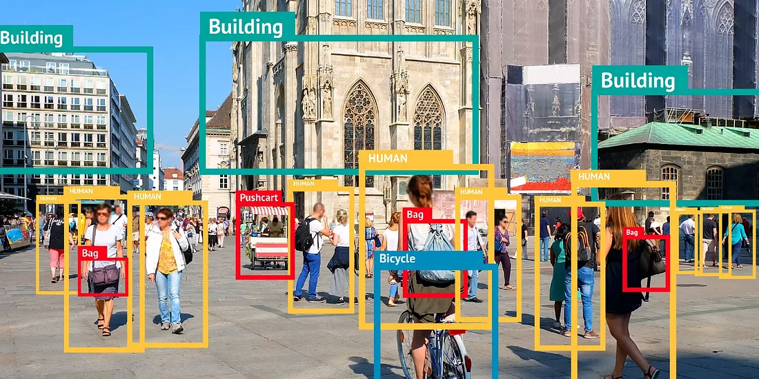 An example of object detection in a busy city square, where people, buildings, bags, and a bicycle are identified using colored bounding boxes and labels for AI training