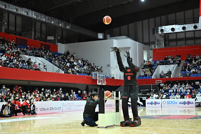 Toyota's CUE AI robot on a basketball court, shooting a basketball with perfect form in front of a crowd