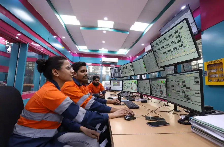 Workers in a modern industrial control room monitoring complex processes on multiple large computer screens for plant operations